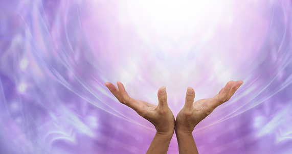 Female hands outstretched sending healing into the light above and an ethereal purple energy formation background