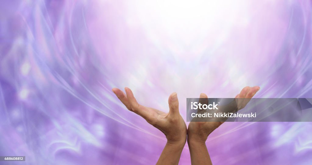 Sending Distant Healing into the Light Female hands outstretched sending healing into the light above and an ethereal purple energy formation background Miracle Stock Photo