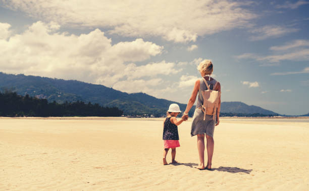 istock Mother and daughter walking on sandy beach 688725360