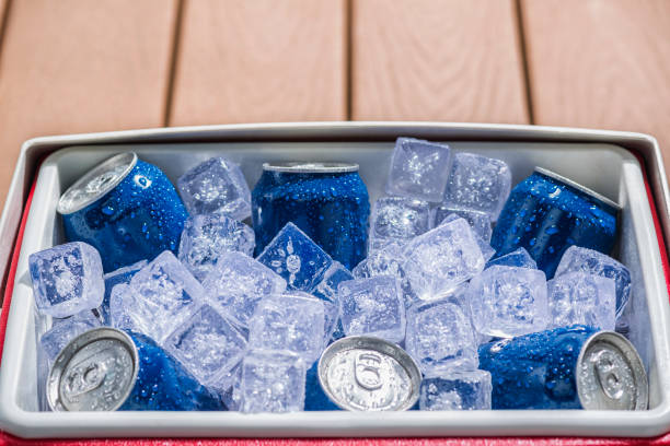 Cooler full of ice cold drinks cans Looking down on a red and white personal cooler with a six pack of blue aluminum cans on ice sitting on a deck outside. These cans can be either soda, beer or other beverage. drinks on the deck stock pictures, royalty-free photos & images
