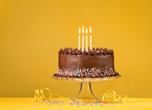 Chocolate birthday cake with colorful sprinkles and candles over yellow background.