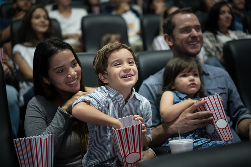 Portrait of a happy Latin American family at the movies eating popcorn and having fun
