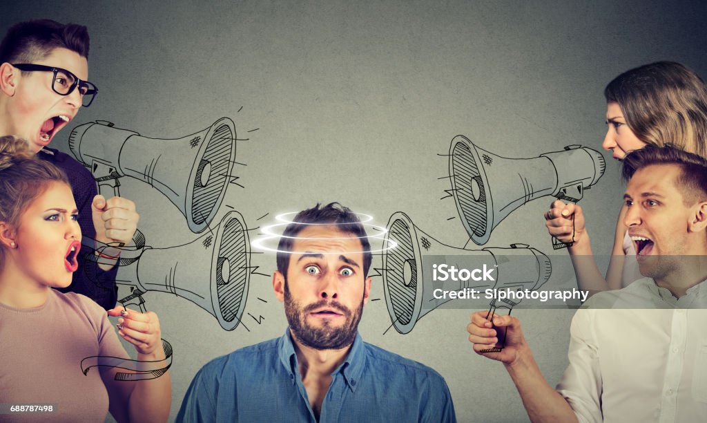 Group of people screaming in megaphones at scared guy Emotional Stress Stock Photo