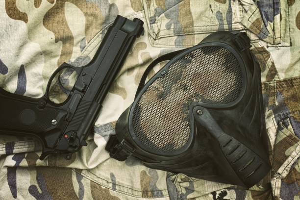 maschera di protezione airsoft, maschera terroristica e pistola da 9 mm (pistola m9) su sfondo mimetico. - m9 foto e immagini stock