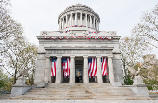 This is a horizontal, color photograph of Grant's Tomb, known known as the General Grant National Memorial. The neoclassical architecture is located in Manhattan's Riverside Park. American flags hang between the columns at the entrance. Photographed with a NIkon D800 DSLR camera.
