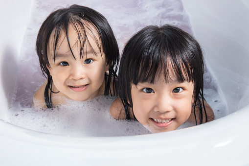 Asian little Chinese girls playing with water and foam in bathtub at home