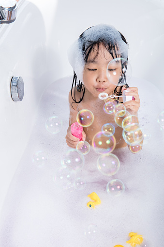 Asian little Chinese girl blowing bubbles in bathtub at home