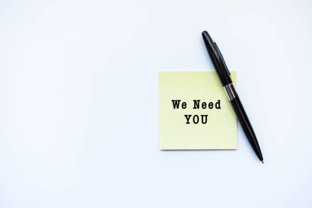 istock WE NEED YOU word concept on sticky note and a pen over top view flat lay isolated on white background. 688831580