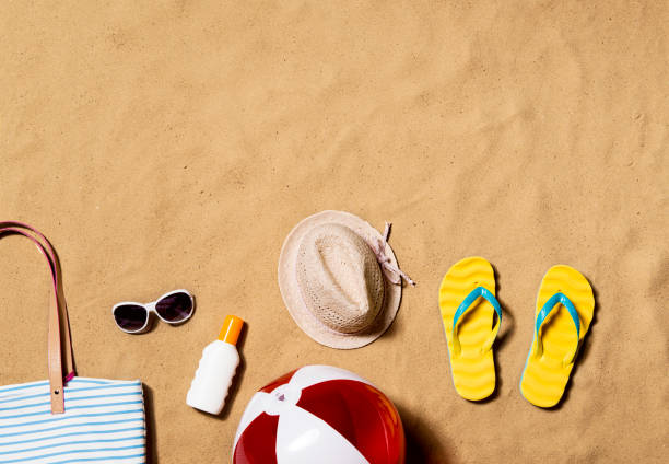 Summer vacation composition. Flip flops, hat and other stuff Summer vacation composition with pair of yellow flip flop sandals, hat, sunglasses, sunscreen and other stuff on a beach. Sand background, studio shot, flat lay. Copy space. beach bag stock pictures, royalty-free photos & images