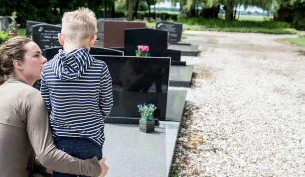 Closeup header image with copy space of a widow mother and her son visiting the cemetery.