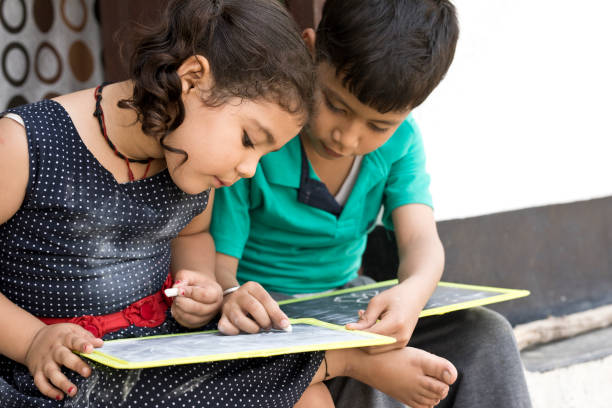 Indian boy and girl writing on slate outdoors