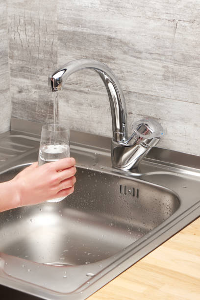 istock Female hand holding glass under tap water against kitchen sink 688879254