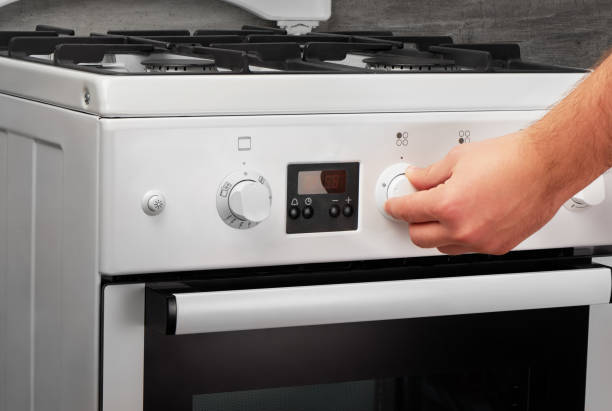 istock Male hand turning on white stove on gray background 688879332