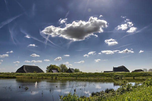 Clouds and Contrails Mostly blue sky with scattered clouds and contrails over a landscape with a shallow pond and several farm buildings on the island of Tiengemeten tiengemeten stock pictures, royalty-free photos & images