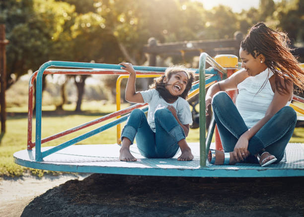 Enjoying some quality time out in the lovely sunshine Shot of a mother and her daughter playing together on a merry-go-round at the park playground stock pictures, royalty-free photos & images