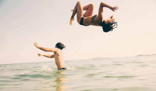 Woman doing a backflip off man's shoulders into the sea.