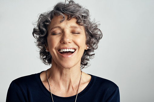 Studio shot of a happy mature woman laughing against a gray background