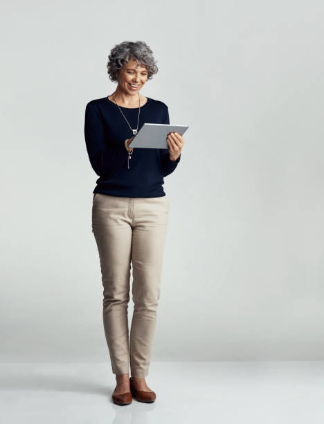 Tapping into the world wide web Studio shot of a mature woman using a digital tablet against a gray background old woman smiling tablet stock pictures, royalty-free photos & images
