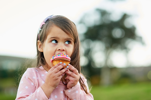 Cropped shot of a little girl enjoying a cupcake outside