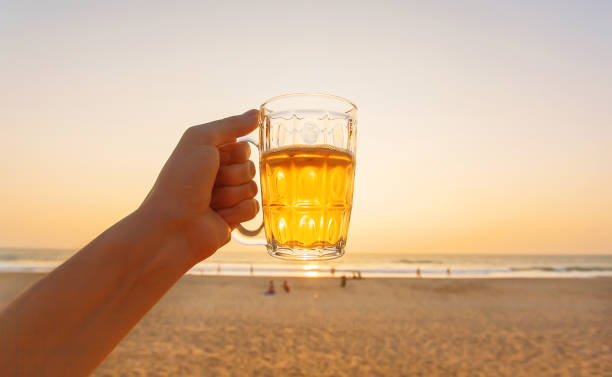 Beer mug in tourist hand with seaside background and sunset beach
