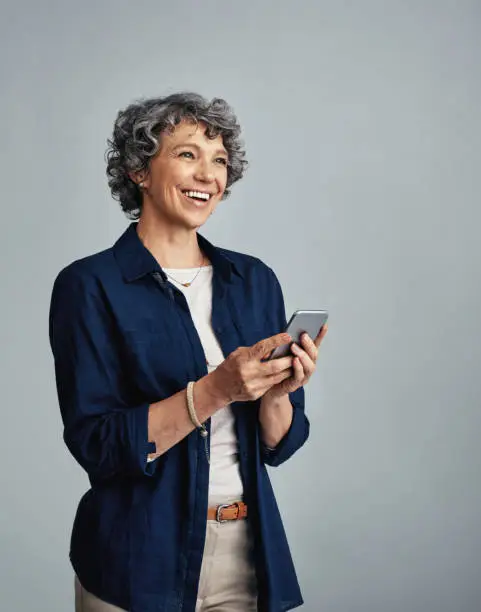 Studio shot of a mature woman using a mobile phone against a gray background