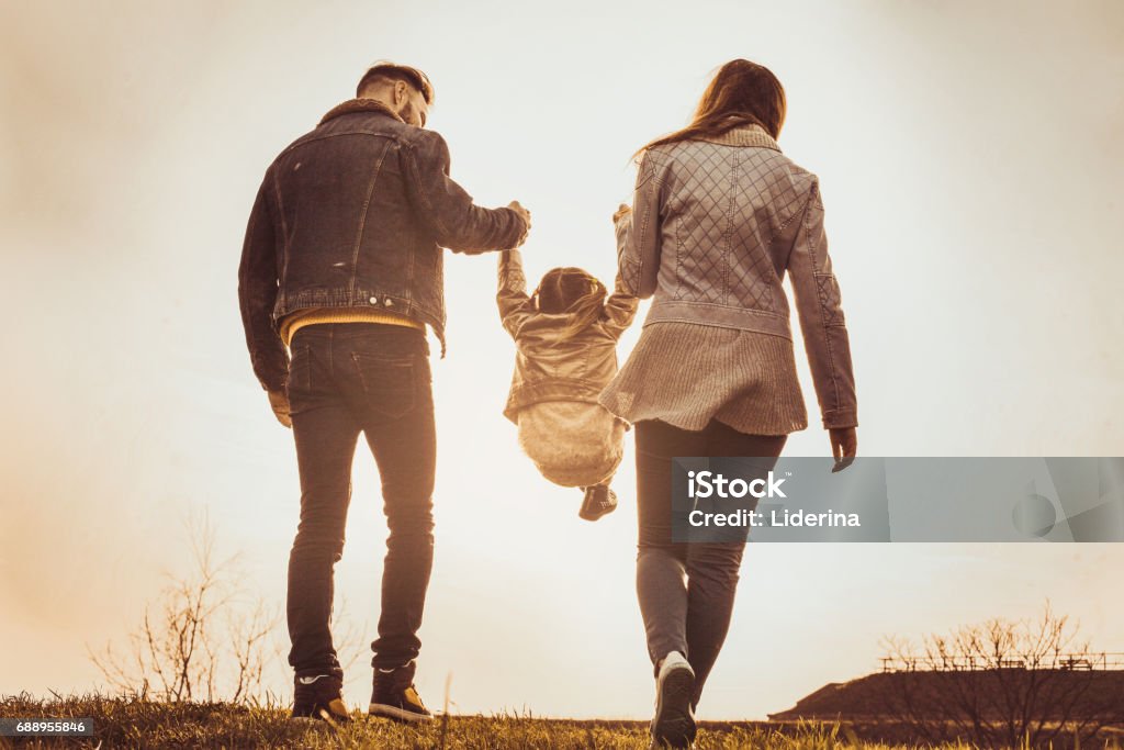 Padres felizes jugando con su hija en el parque. Los padres elevar en el aire una niña. - Foto de stock de Vista posterior libre de derechos