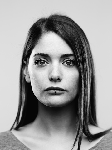 Close-up back and white portrait of confident real young woman with long hair. Beautiful female is against white background. Vertical studio photography from a DSLR camera. Sharp focus on eyes.