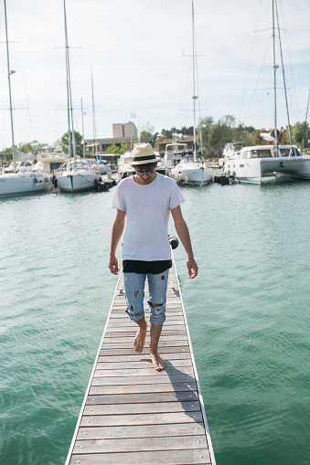 Young and beautiful hipster man walking on the pier in the marina