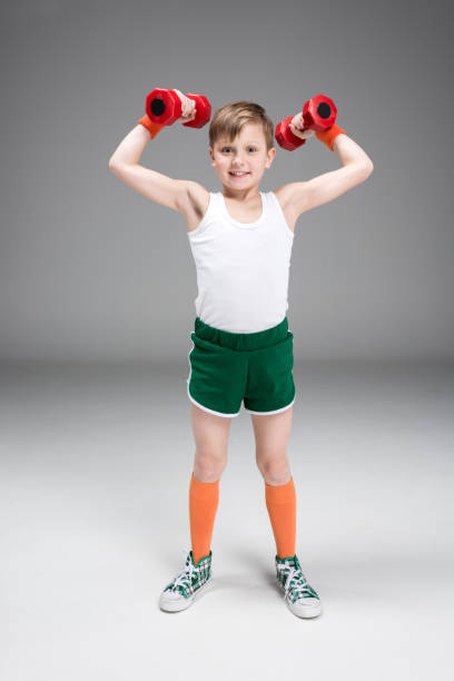 istock smiling active boy holding dumbbells isolated on grey 688958878
