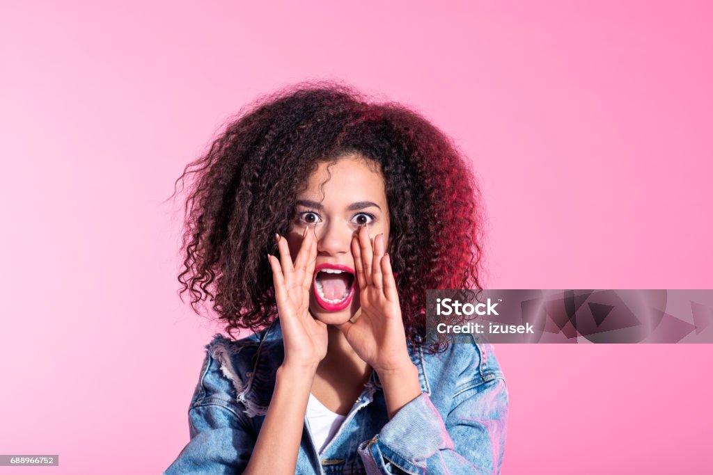 Surprised young afro woman shouting Studio portrait of cute young afro woman shouting at the camera. Pink background. Adult Stock Photo