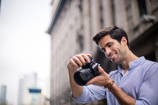 One man, standing outdoors on the street, holding a camera and taking pictures.