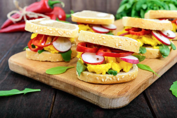 istock Sandwich with scrambled eggs, rucola, radish, paprika kapi and flax seeds on a cutting board on a dark wooden background. Fast and tasty breakfast. 688974252