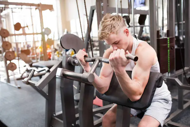 Photo of Young man in gym working out, using weights machine for arms.