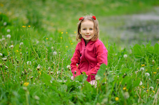 A girl is sitting in the grass on the bank of a lake, a river. The child looks seriously at the lens. Concentrated look, curly hair, fleece jacket.. Children Protection Day.