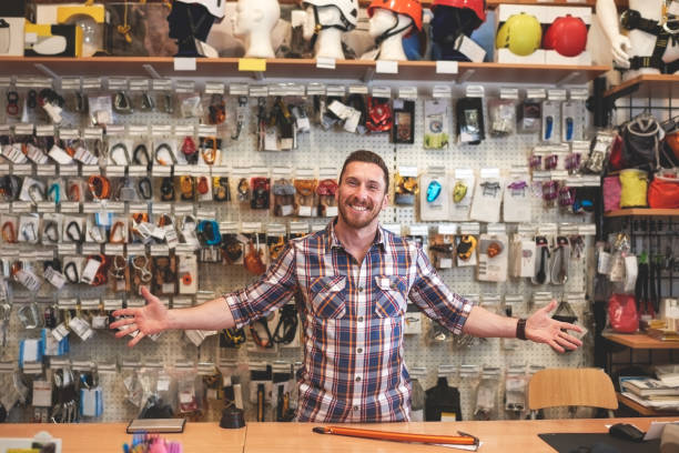 Male sales person is standing in sports and outdoor equipment store and greeting customers with a smile.