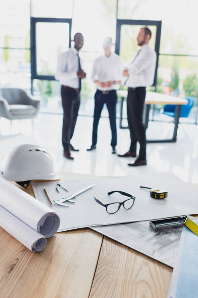 istock various architecture supplies on workplace with architects behind, focus on foreground 688999696