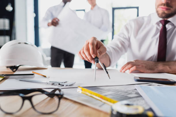 istock partial view of architect working on new project with colleagues behind in modern office 689001278