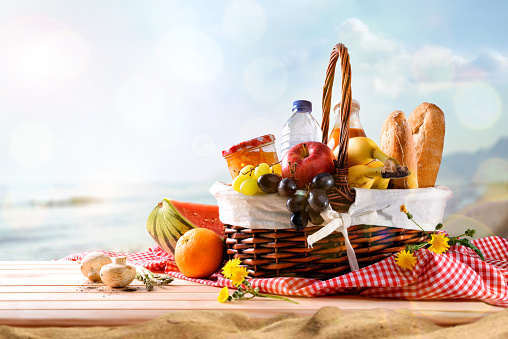 Picnic wicker basket with food on table on the beach