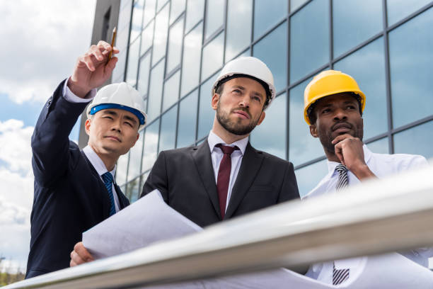 istock Multiethnic group of professional architects in helmets working with blueprint outside modern building 689010848