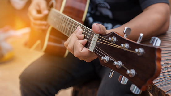 Caucasian male music teacher, playing acoustic guitar, while leading a class with female student