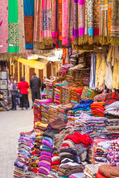 colorful fabrics and carpets for sale on a street in medina of essaouira, morocco - craft market morocco shoe imagens e fotografias de stock