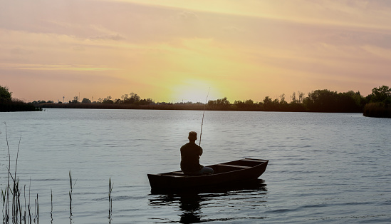 Fisherman on fishing boat in river at sunset