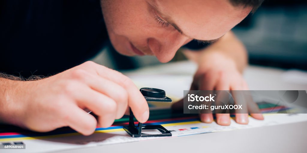 Worker in printing and press centar uses a magnifying glass Worker in a printing and press centar uses a magnifying glass and check the print quality Printing Press Stock Photo