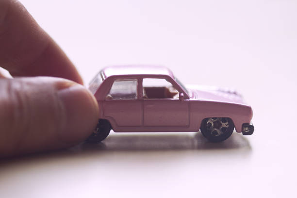 front view closeup of mature hand pushing a little miniature pink toy car on light background