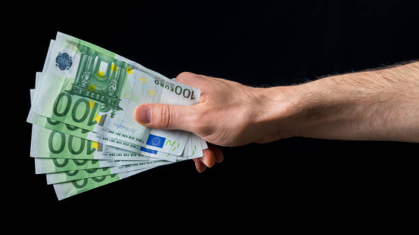 holding money of European currency euro. give 100 euro money, hand holding one hundred euro cash isolated on a black background netherlands currency stock pictures, royalty-free photos & images