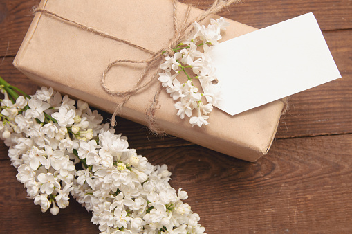 A bouquet of white lilac on a wooden table with a gift box there is a label for the inscription