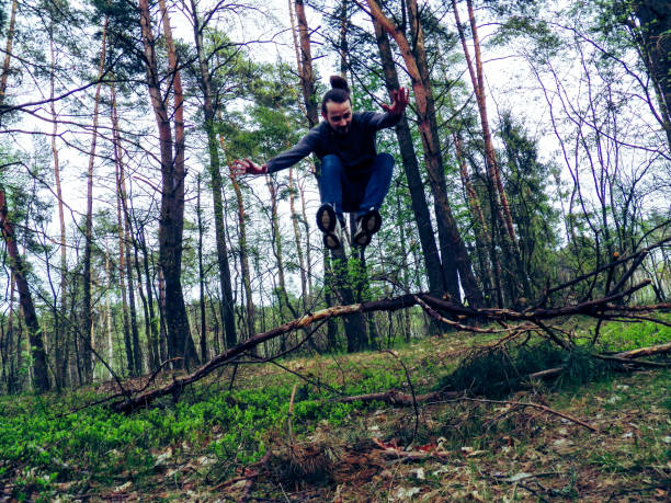 istock Bearded hipster jumping over a tree in the forest. Low angle view. 689142856