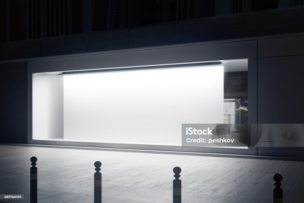 Shopfront with white billboard side Side view of empty glass shopfront with blank white billboard at night. Retail  concept. Mock up, 3D Rendering Store Window Stock Photo