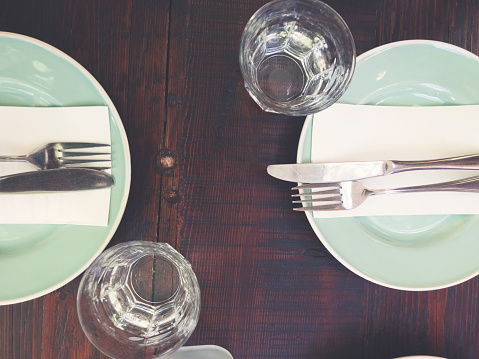 Two place settings on a wooden table. There is cutlery, plates and napkins with water glasses.