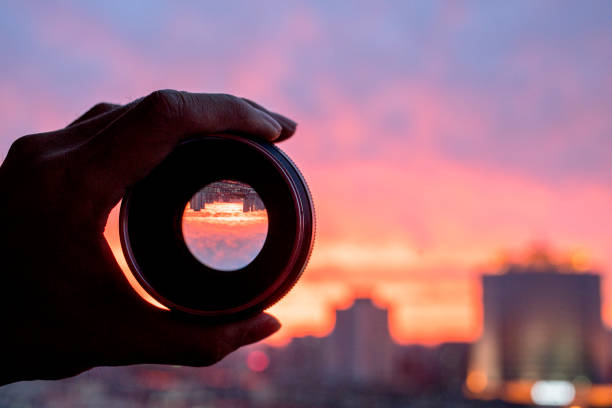 mão segurando a lente da câmera, olhando scenics de nuvens brilhantes ao pôr do sol - lens camera focus photography - fotografias e filmes do acervo